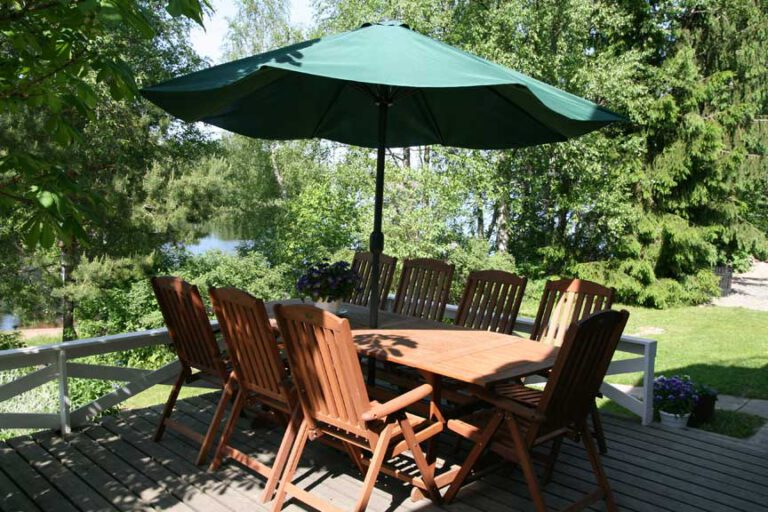 A wooden dining table, chairs and a green parasol on the terrace.